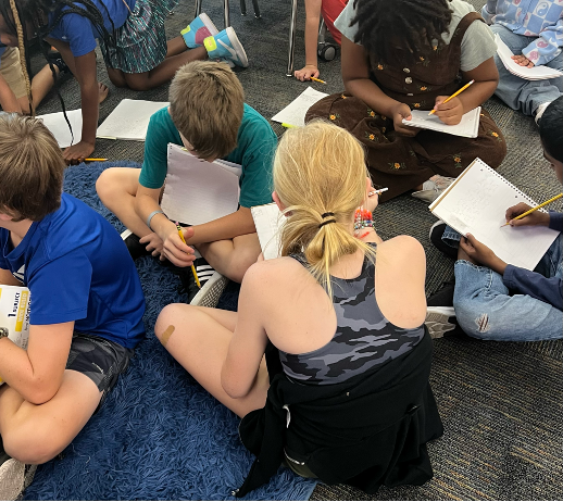 Students sit on a rug, brainstorming ideas for writing during a Being a Writer lesson.