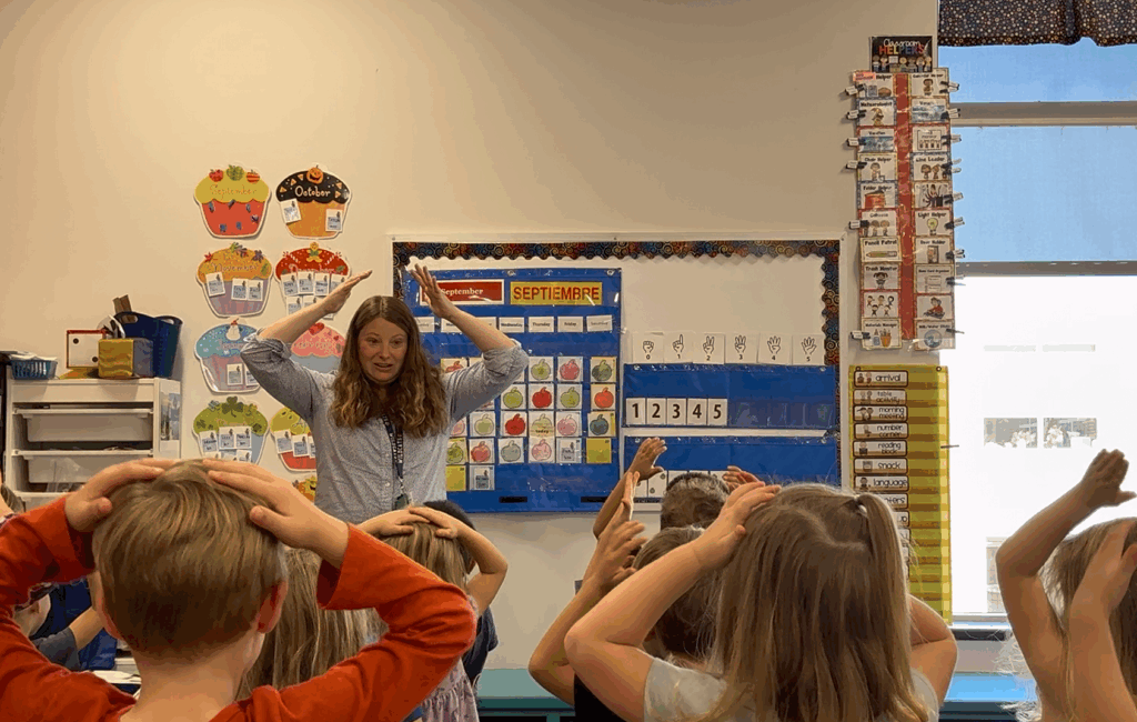 Belleville School District Pre-K teacher Jamie Bell leads her class in a Pinecone Path routine. In this photo she is holding her hands above her head and the children are standing in front of her, copying her actions.
