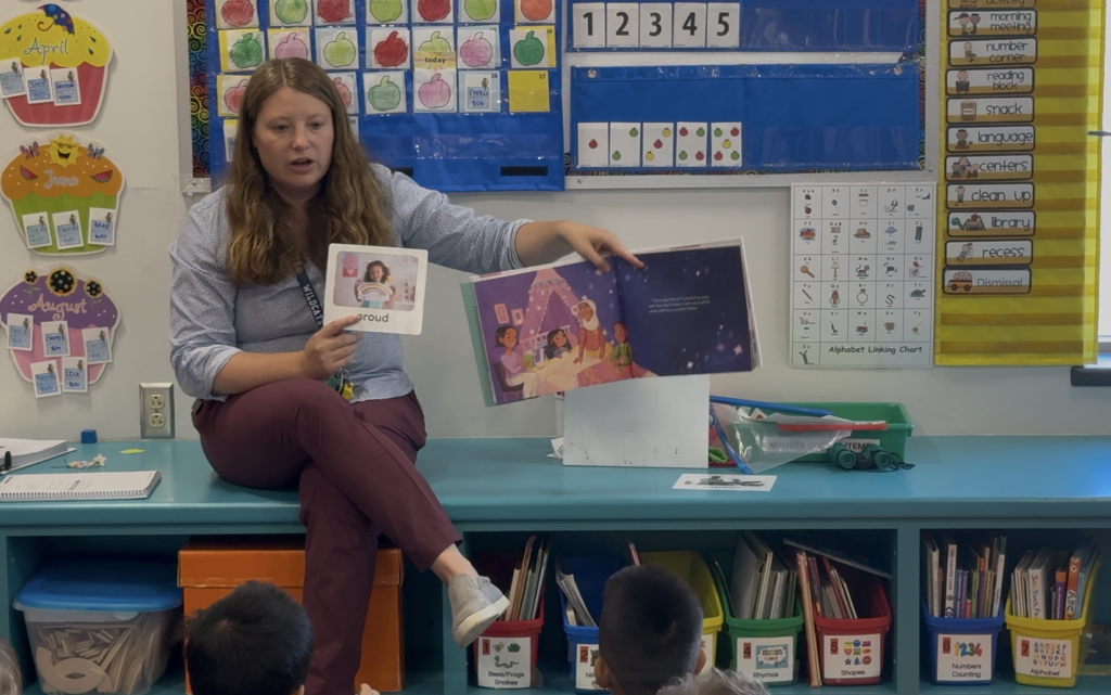 Belleville School District Pre-K teacher Jamie Bell is sitting in front of her classroom of students, holding up a book for them to see during a repeated read aloud.