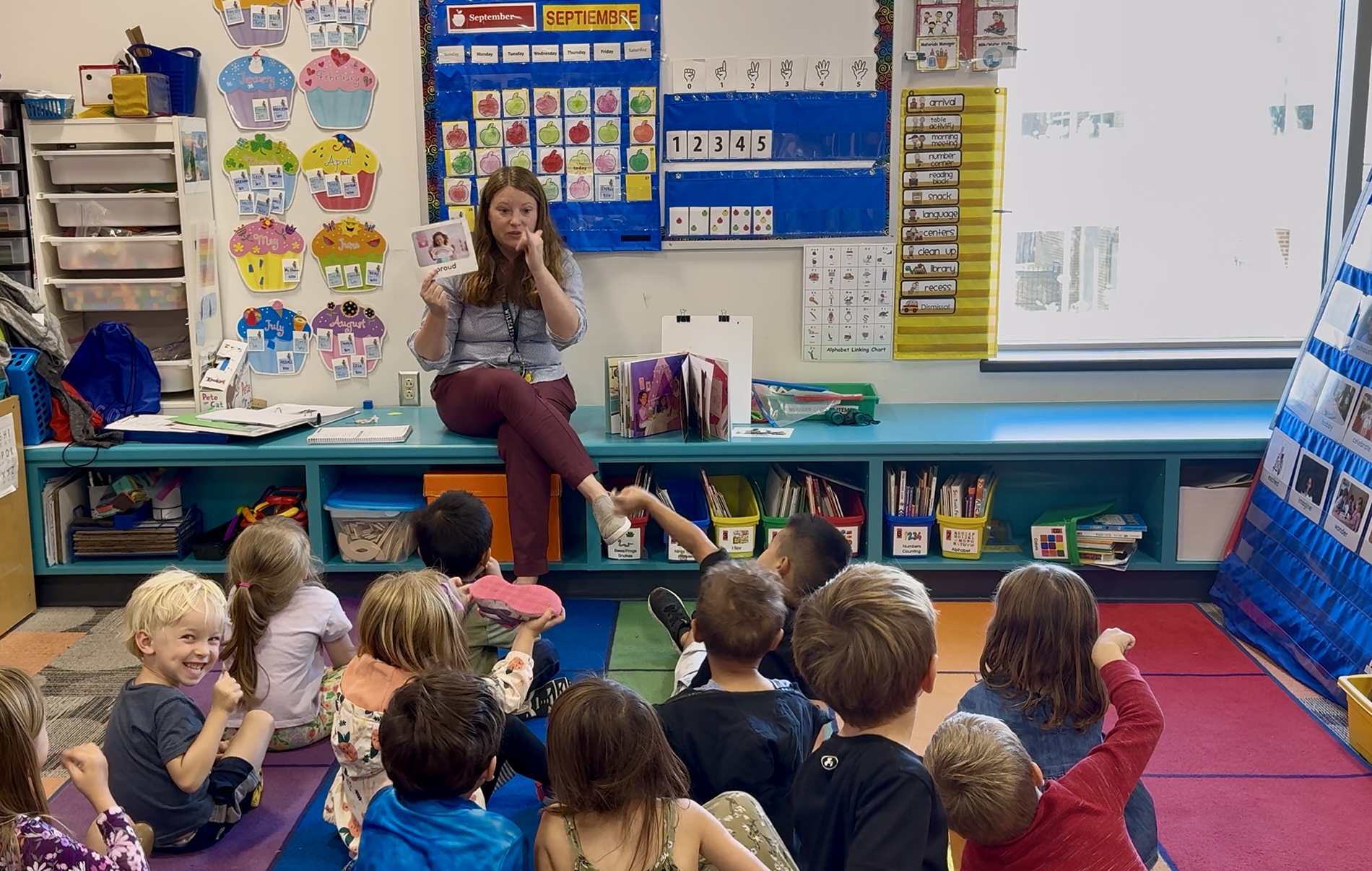 Belleville pre-k teacher sits in front of a classroom of students sitting on the floor facing her while she reads them a book.