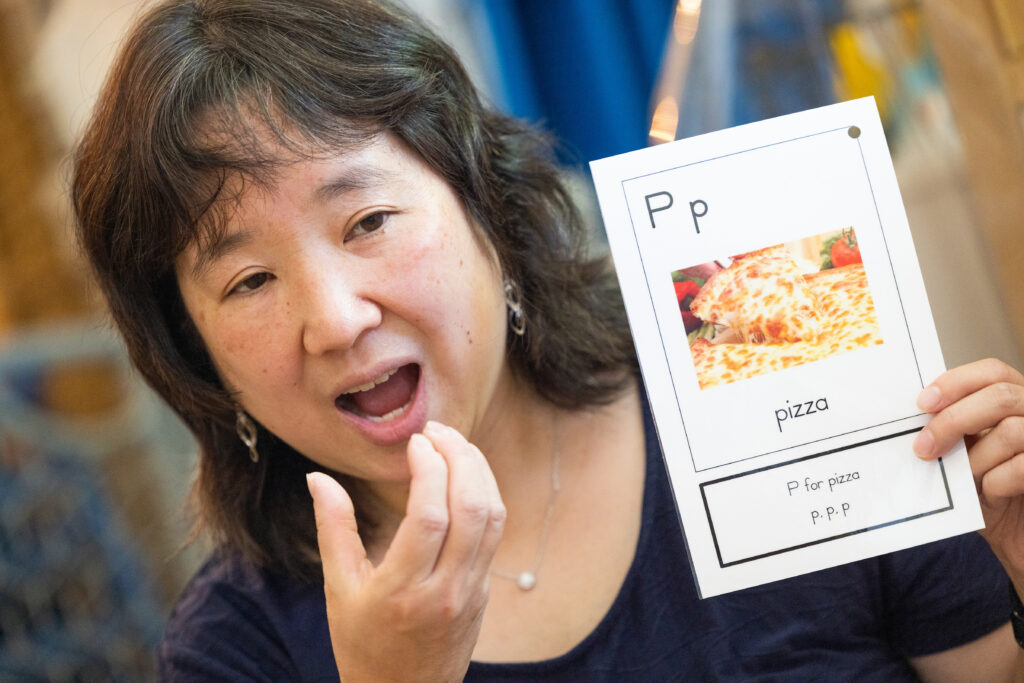 Preschool educator focused on teaching phonological awareness holding a letter card with the letter "P" and an image of a pizza followed by the word, "pizza".