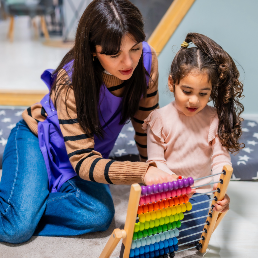 A woman and young child sit together on a carpeted floor using an abacus to count.