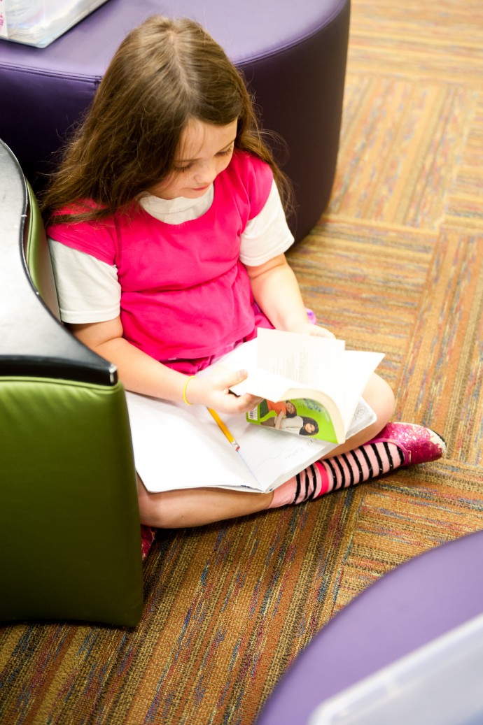 student sitting on classroom floor, reading a book