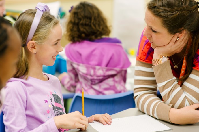 student with pencil at desk, talking with her teacher